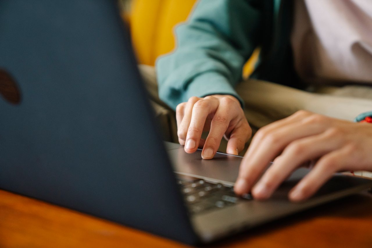 Hands typing on a laptop keyboard with a wooden surface beneath the device.