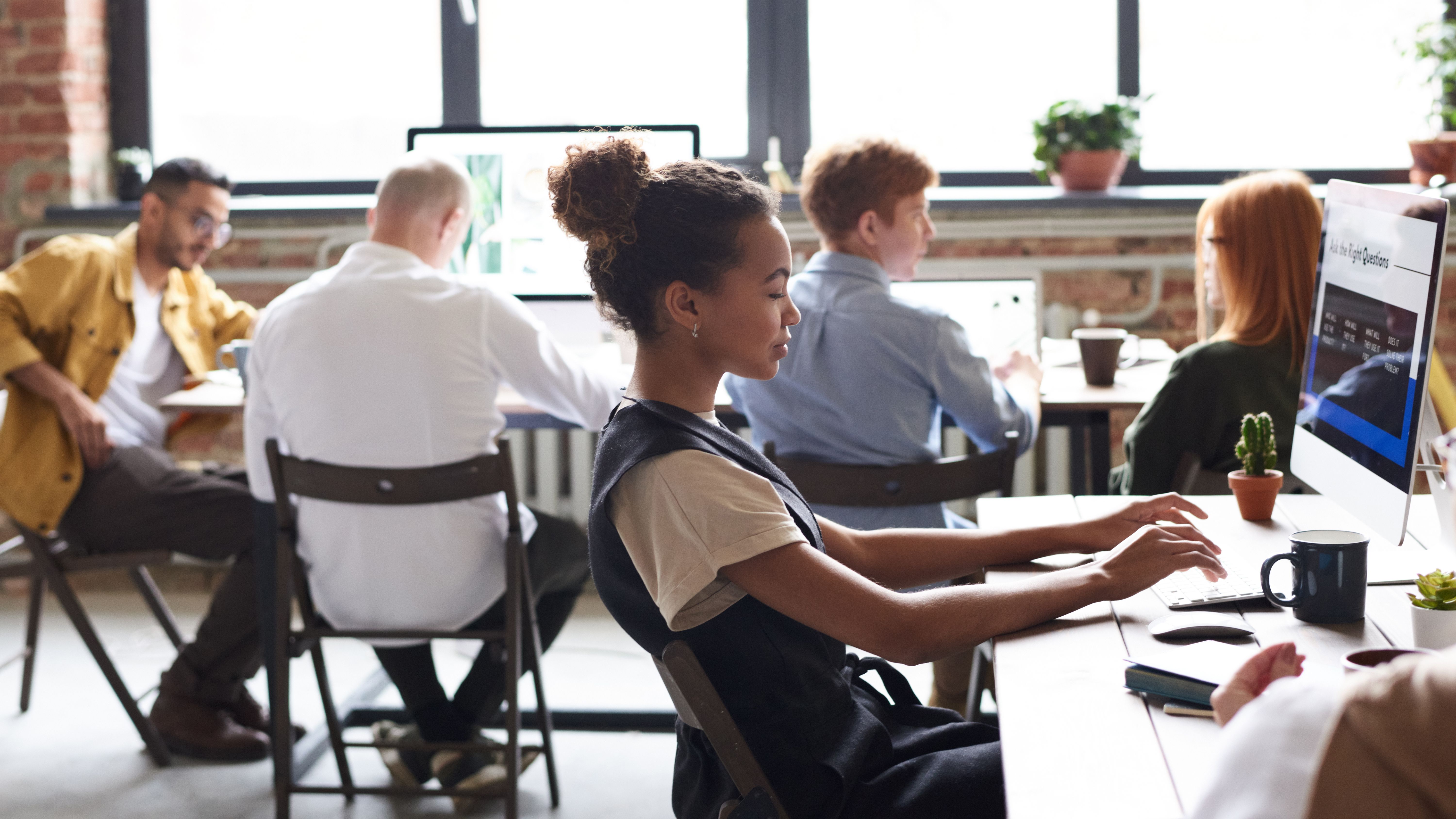Young professionals working on computers in a bright modern office with plants and large windows.