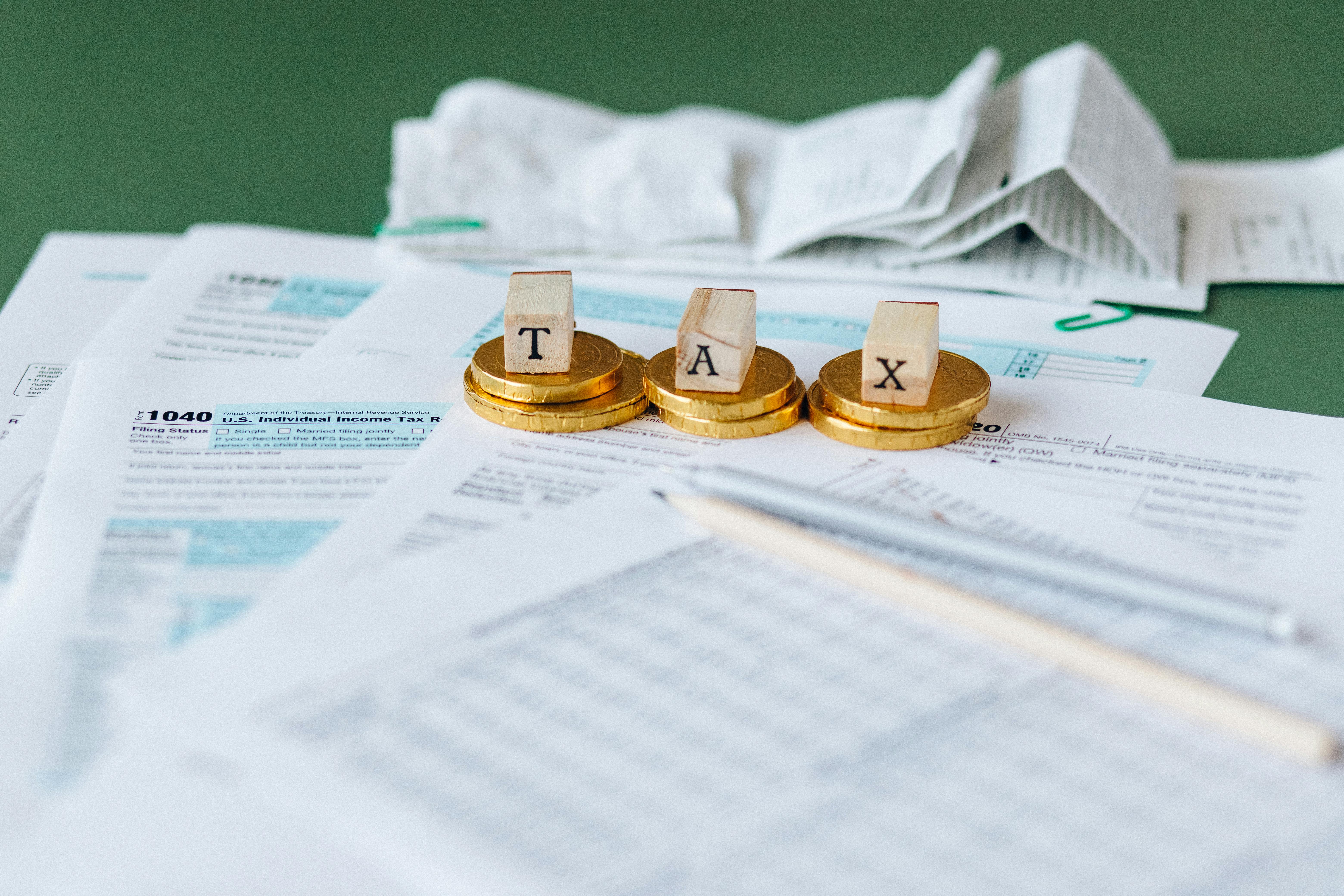Wooden blocks spelling TAX on gold coins over U.S. income tax forms with pencil and receipts.
